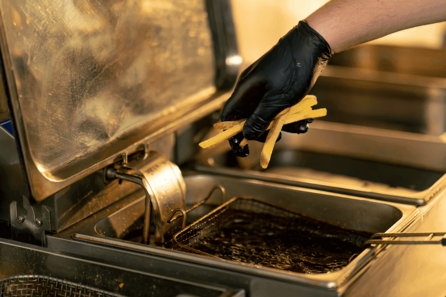 A chef in black gloves carefully adds fries to a commercial deep fryer, showcasing the professional kitchen environments Renova supports.