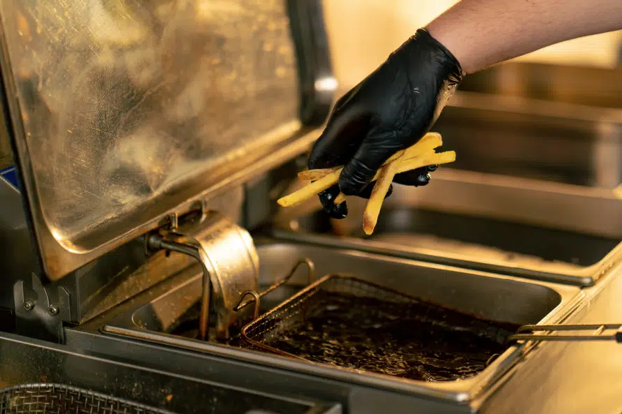professional-cooking-oil-collection-service.jpg A chef in black gloves carefully adds fries to a commercial deep fryer, showcasing the professional kitchen environments Renova supports.